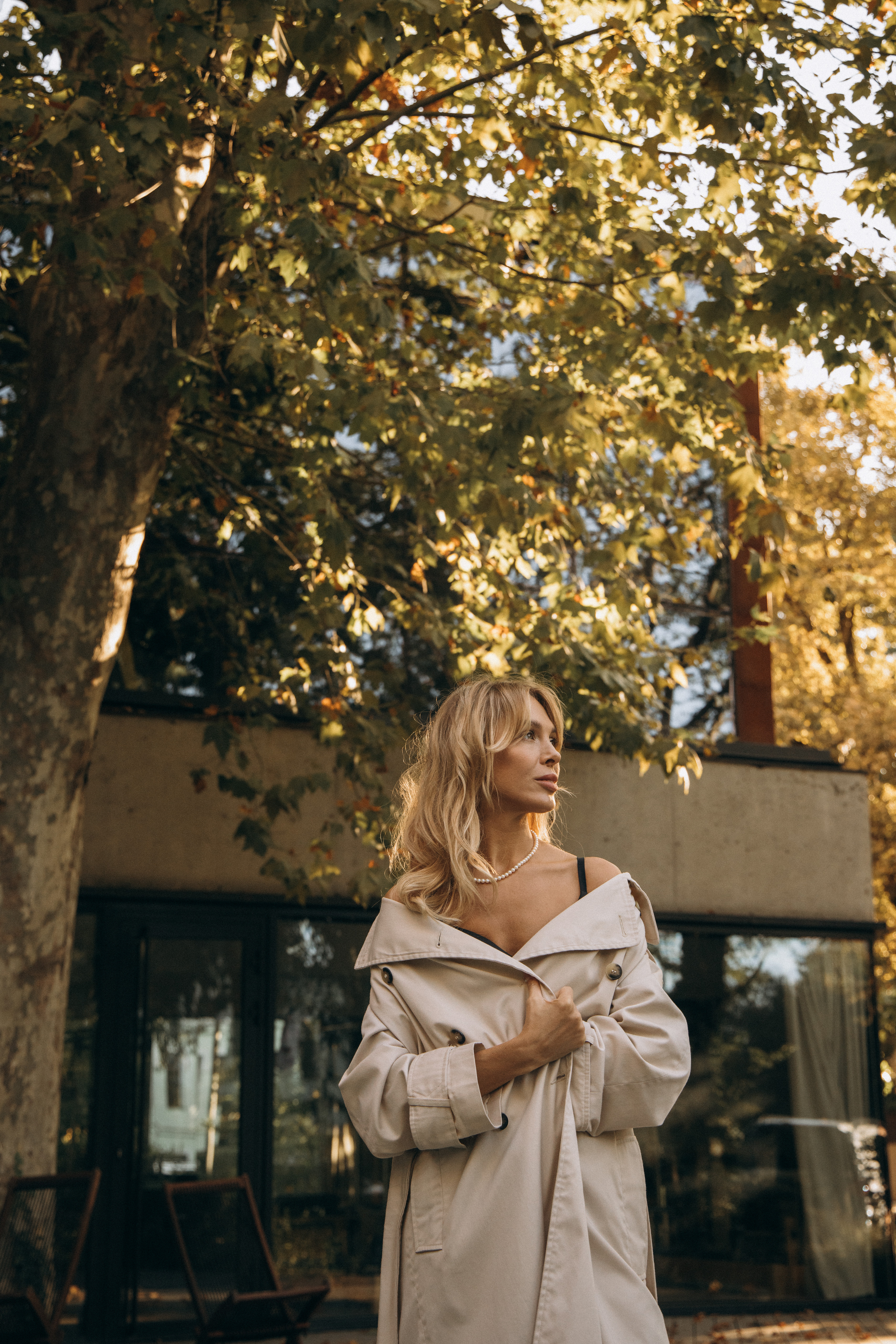 Woman in beige coat near autumn foliage.